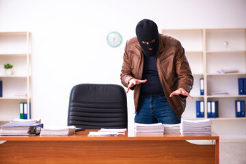 Young man in balaclava stealing information from the office