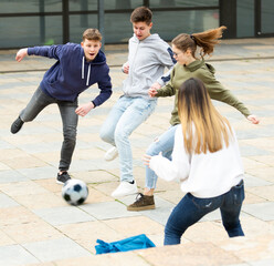 Cheerful schoolchildren are playing football in the school yard during a break in casual clothes