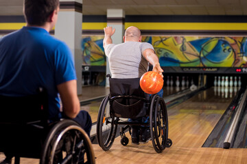Two young disabled men in wheelchairs playing bowling in the club