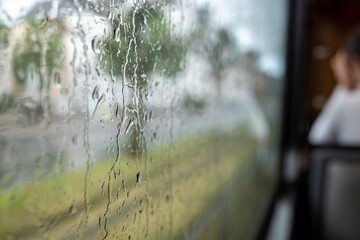 Close-up and macro view of raining water drop on outside windows of the tram or train and defocused background of indoor passenger train. 