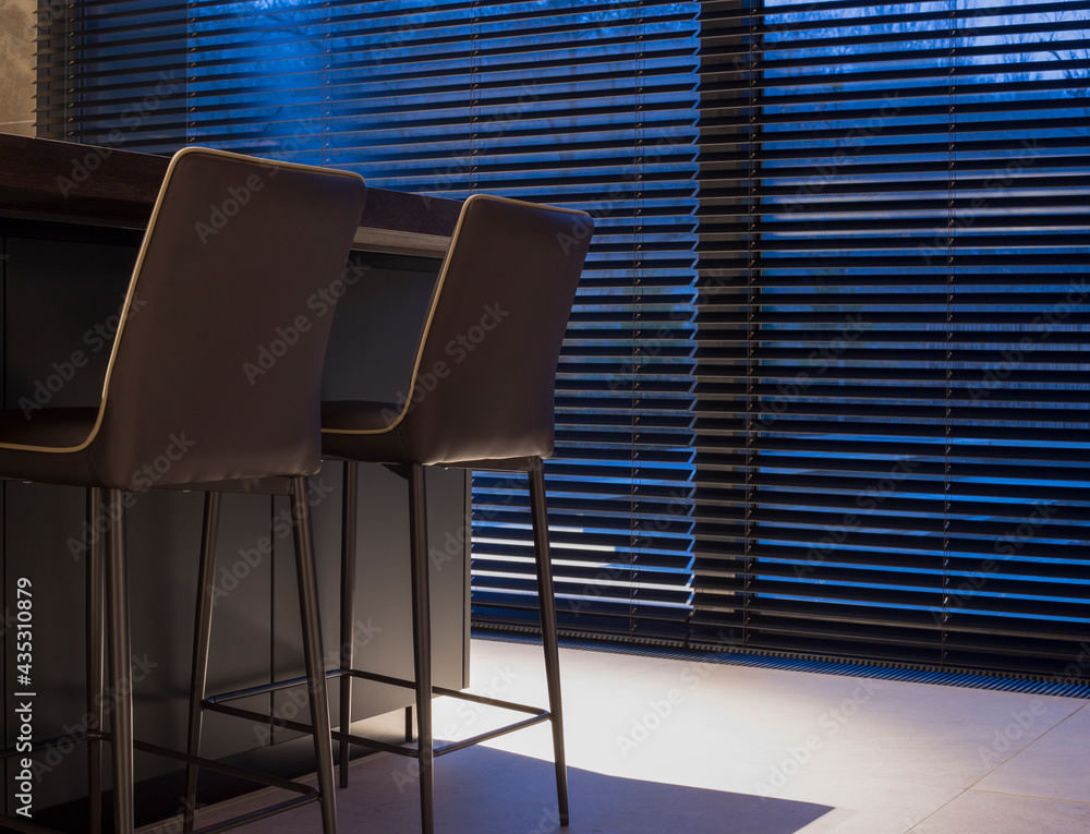 Poster wood blinds black color on large windows in the interior. next to the window is a table with chairs.