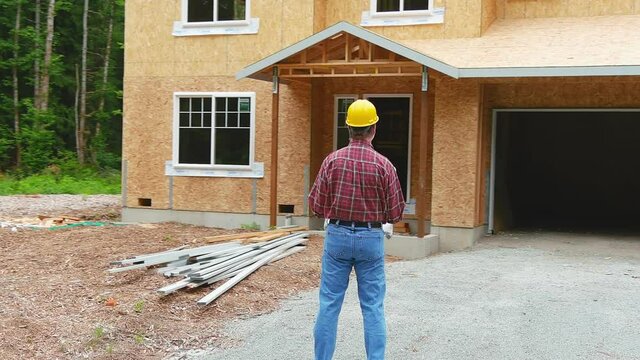Construction worker standing in front of an unfinished new construction home holding a set of plans reviewing progress