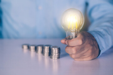 Hands of businessman holding light bulb while coin on desk, saving and finance for success, knowledge about deposit and earning and investment, solution and inspiration, business concept.