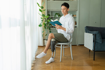 窓際で本を読む義足の男性