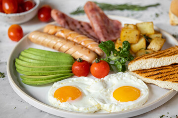 English breakfast menu with fried eggs,ham,avocado-slices ,deep fried potatoes,sausage and tomato