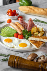 English breakfast menu with fried eggs,ham,avocado-slices ,deep fried potatoes,sausage and tomato