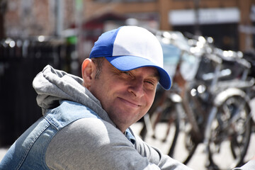 Man is sitting on a curb on city street smiling and looking into camera