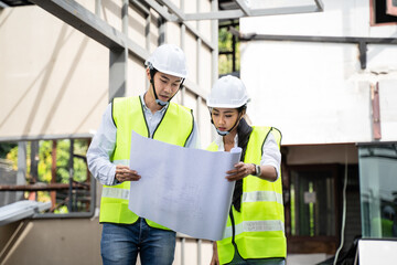 Asian male architect explaining job on blueprint to his colleague.