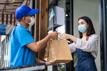 Asian waitress wearing face mask, handing takeaway bag to delivery man	