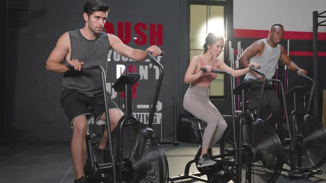 Multiethnic athlete group doing exercise by spinning assault air bike.