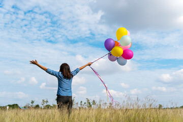 Woman holding balloons running on green meadow white cloud and blue sky with happiness Cheerful and relax. Hands holding vibrant air balloons play on birthday party happy times summer sunlight outdoor