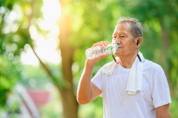 Asian elderly man or senior runner Tired from running and exercising Drinking water to rest From outdoor jogging and walking in the park