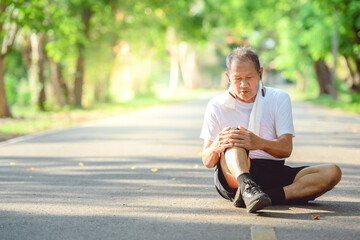 Asian elderly man or senior runner Stop running because of a knee injury. And put a hand on the...