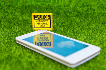 Caution sign with smartphone on green grass background, information security, phone safety,...