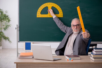 Old male teacher holding line in front of blackboard