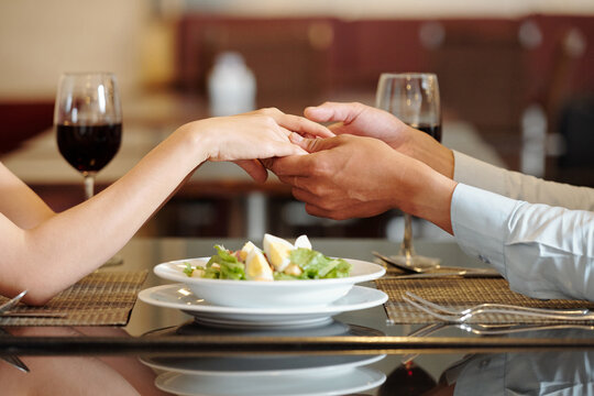 Close-up image of young couple holding hands over plate of salad on restaurant table