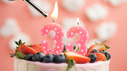 Birthday cake number 33, pink candle on beautiful cake with berries and lighter with fire against...