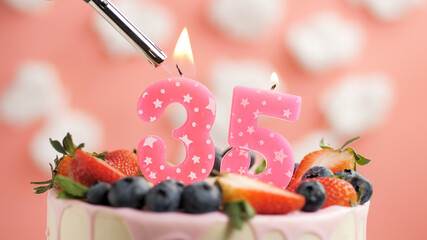 Birthday cake number 35, pink candle on beautiful cake with berries and lighter with fire against...