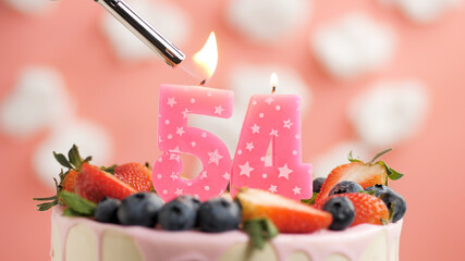 Birthday cake number 54, pink candle on beautiful cake with berries and lighter with fire against...