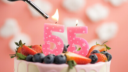 Birthday cake number 55, pink candle on beautiful cake with berries and lighter with fire against...