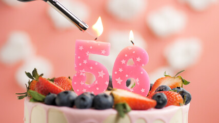 Birthday cake number 56, pink candle on beautiful cake with berries and lighter with fire against...
