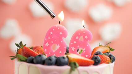 Birthday cake number 66, pink candle on beautiful cake with berries and lighter with fire against...