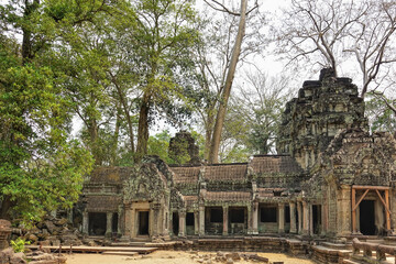 Fototapeta premium The ancient temple of Angkor is dilapidated. Colonnades, empty doorways are visible. Carvings and ornaments on the stones. Jungle all around. Branches of trees against the sky. Cambodia