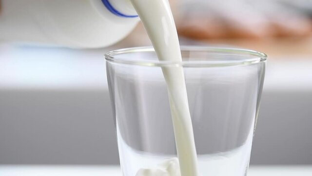Pouring milk from plastic bottle into a glass in the kitchen, slow motion