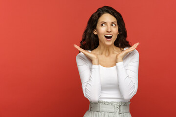 Portrait of surprised woman with open mouth hands gesturing looking aside to copy space for...