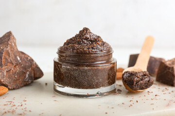 Jar of chocolate body scrub and ingredients on light background