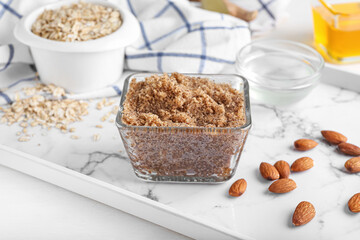 Bowl of natural body scrub and ingredients on light background