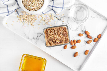 Bowl of natural body scrub and ingredients on light background