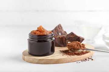 Jar of chocolate body scrub and ingredients on light background