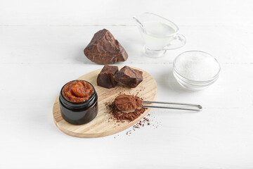 Jar of chocolate body scrub and ingredients on light wooden background