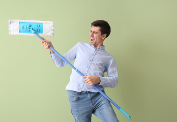 Young man with floor mop on color background