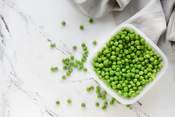 Plastic container with green peas on light background