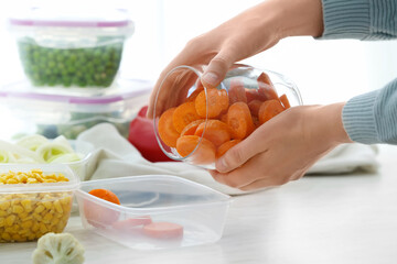 Woman putting carrots into plastic container in kitchen, closeup