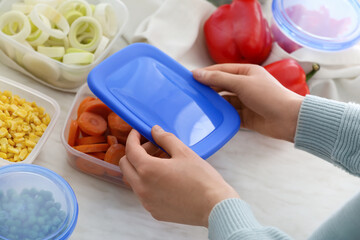 Woman closing plastic container with carrots in kitchen, closeup