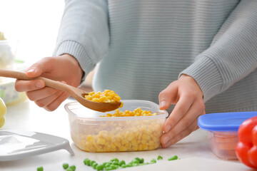 Woman and plastic container with corn in kitchen, closeup