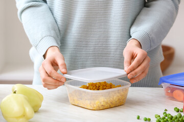 Woman closing plastic container with corn in kitchen, closeup
