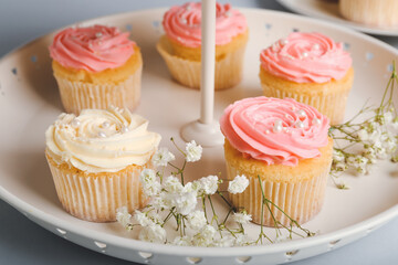 Dessert stand with tasty cupcakes and flowers on table, closeup