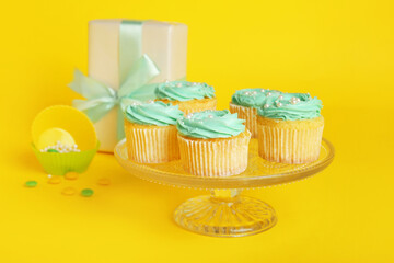 Dessert stand with tasty cupcakes and gift box on color background