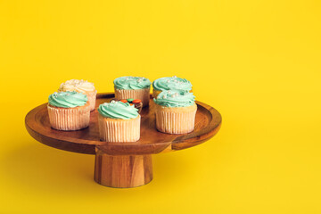Dessert stand with tasty cupcakes on color background