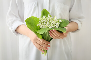Woman with bouquet of beautiful lily-of-the-valley flowers on light background