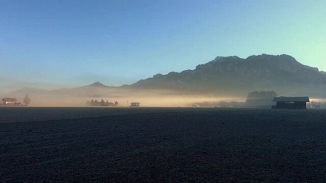 Drone shooting farmland with wooden houses located in valley in foot of mountains, aerial bird's eye view of picturesque rural environment with homestead huts during sundawn