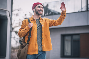 Young man in orange jacket meeting someone and waving his hand