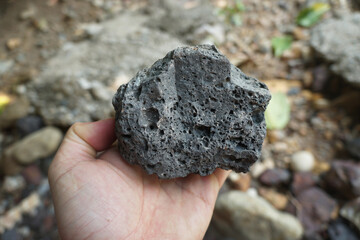 Basalt igneous rock in a hand. Basalt is a dark-colored, fine-grained, igneous rock composed mainly of plagioclase and pyroxene minerals.