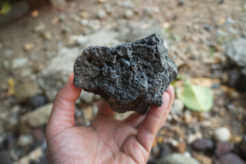 Hand holding a piece of black lava rock.
