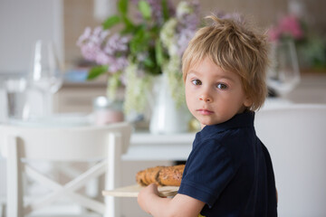 Child, blond toddler boy, holding wooden cutting board with homemade corn bread, serving at home