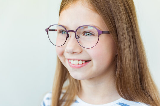 Health care, eyeball check, clear vision concept. Close up portrait of smiling schoolgirl in red and purple glasses